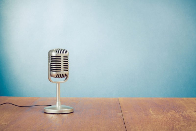 Food Psych. Image of an old-fashioned microphone on a wood table in front of a blue wall.