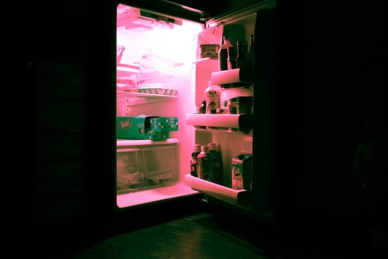 Refrigerator organization is important, and this photos is of an open, cluttered refrigerator in a dark room with a pink glow coming out.