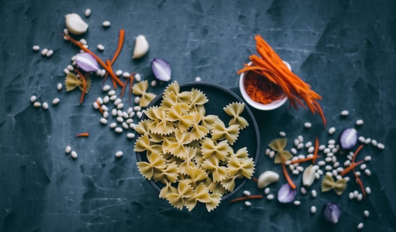 White beans. Flat lay photo of bowtie pasta, dried white beans, garlic cloves and julienned carrots