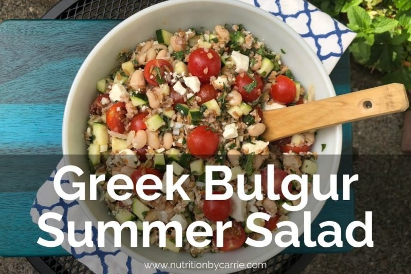 Overhead photo of a large bowl fo Mediterranean bulgur salad, placed on a turquoise-stained wooden cutting board and a Mediterranean-patterned blue and while kitchen towel.