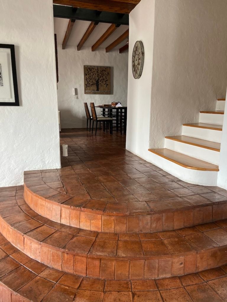 Minimalism: Photo of an apartment with curved, terracotta tiled steps, rustic white walls, and a dining table visible through an open doorway.
