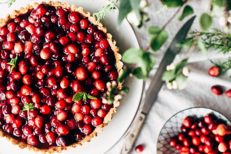 Mindful Eating Holidays: When you approach the holidays mindfully, you can enjoy holiday favorites in a balanced way. Top view photo of a cranberry tart on a white linen tablecloth, decorated with greenery.