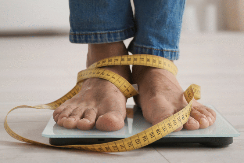 Image of a woman's bare feet, wrapped in a tape measure and standing on a scale.