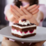 Close up of a piece of birthday cake in front of a woman's hands held up in a "no" gesture