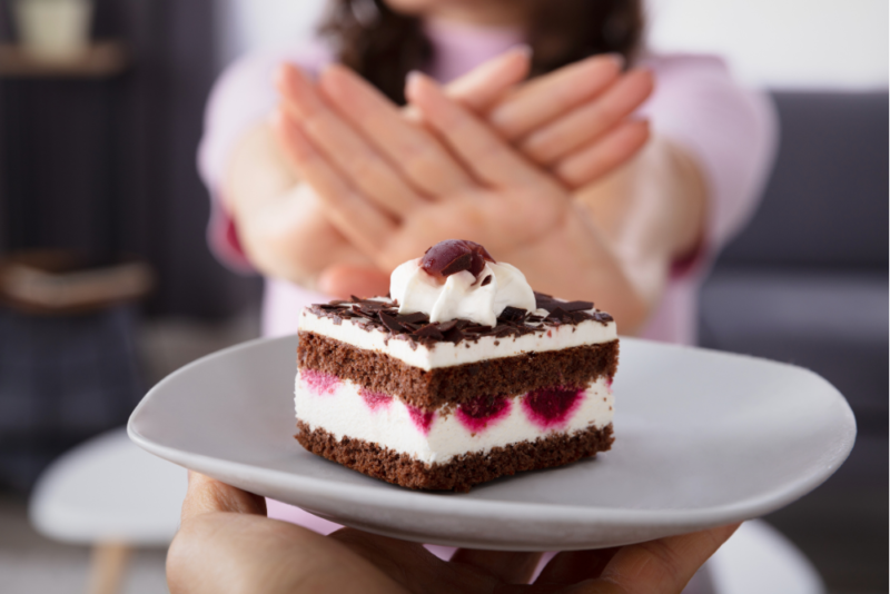 Close up of a piece of birthday cake in front of a woman's hands held up in a "no" gesture